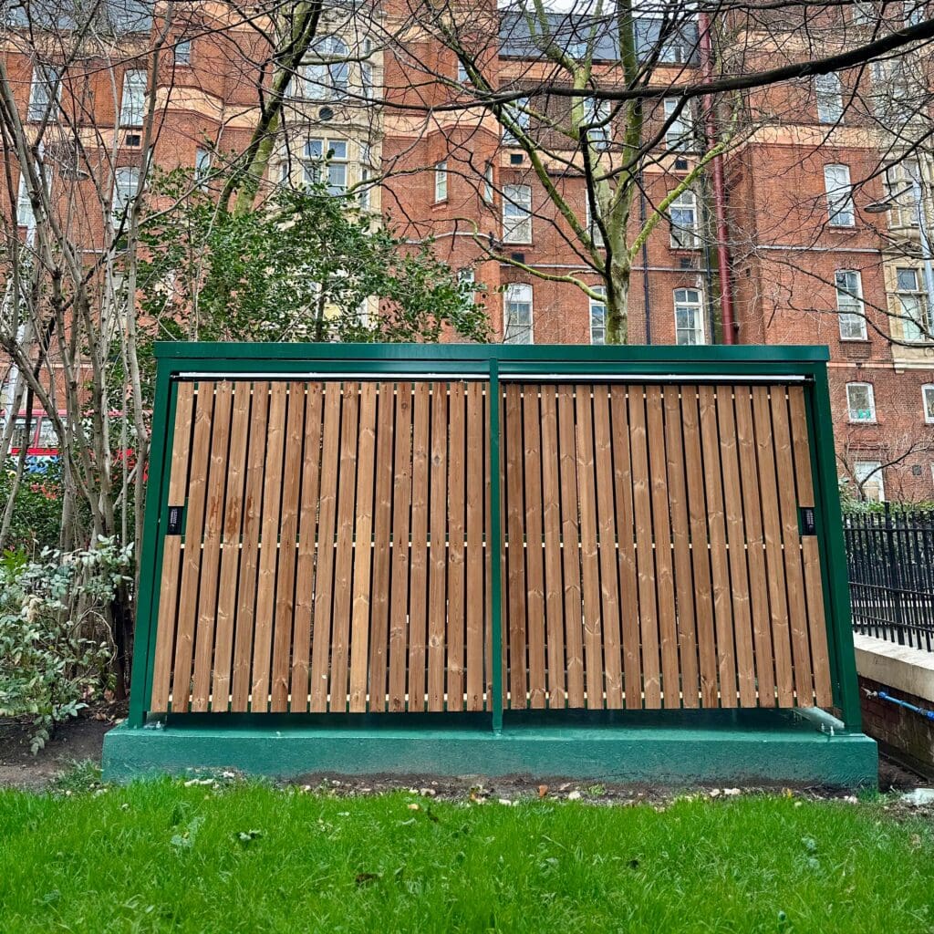 10 Space Amazon Eco Shelter installed at a residential property sitting between the trees with RAL green fascia