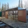A large brown Carlton Shelter bike enclosure stands prominently beside a brick walkway, inviting visitors to explore its surroundings.