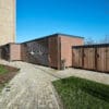 A large brown Carlton Shelter bike enclosure stands prominently beside a brick walkway, inviting visitors to explore its surroundings.