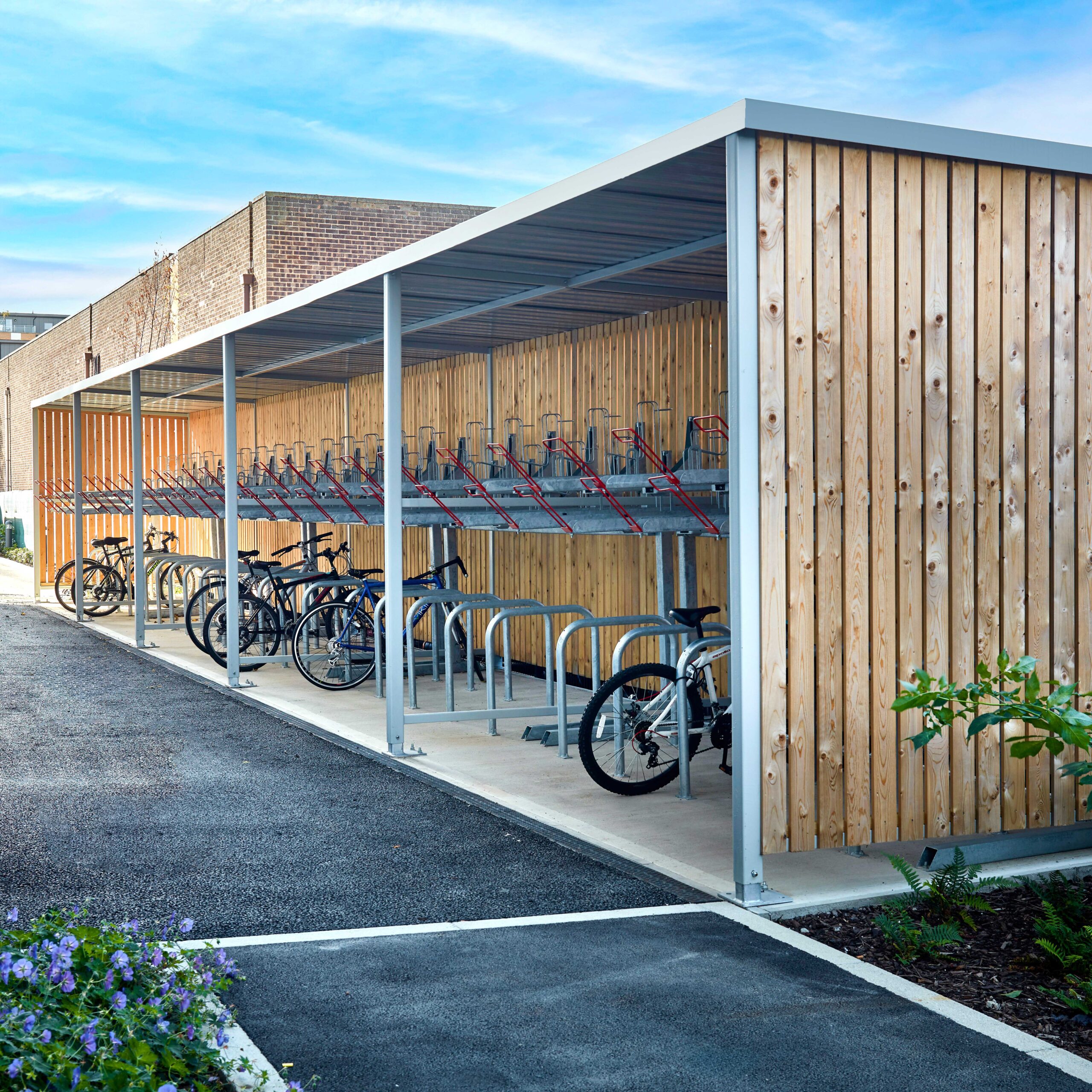 A covered bicycle parking area with empty racks and a few parked bicycles, featuring a wooden back wall and metal supports.