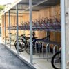A modern, covered bicycle parking area with empty racks and a few parked bicycles, featuring a wooden back wall and metal supports.