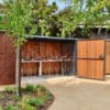 A two-tier wooden cycle shelter with swing doors underneath green trees