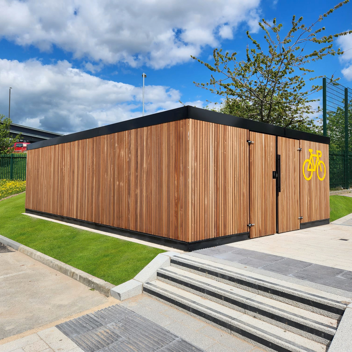 A modern wooden bike shed with a large bicycle symbol, located outside in a sunny environment.