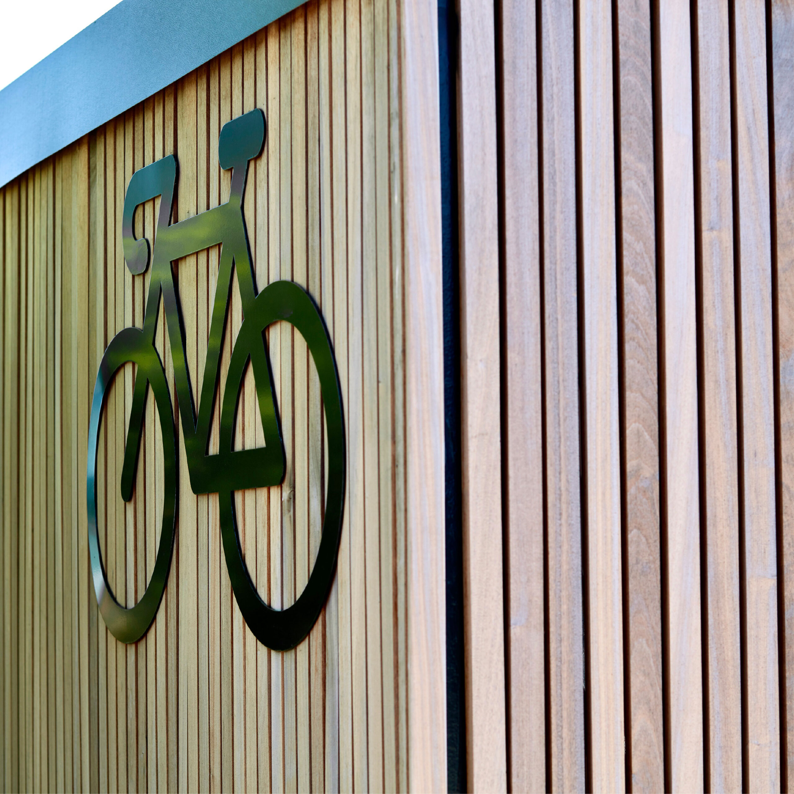 A black bicycle symbol mounted on a wooden slat wall, with part of the sign crossing over onto the slats, creating a clean, modern look.