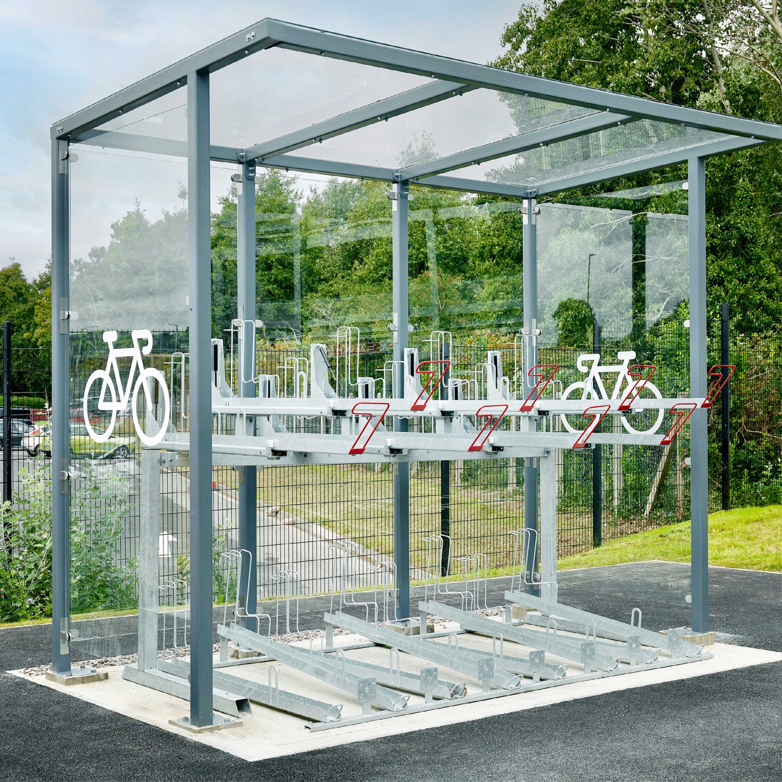 A modern outdoor bicycle parking shelter equipped with secured bike racks and surrounded by greenery and a wooden fence.