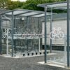 Modern bicycle parking facility with covered bike racks and secured bicycle stands beside a paved road and parking lot.