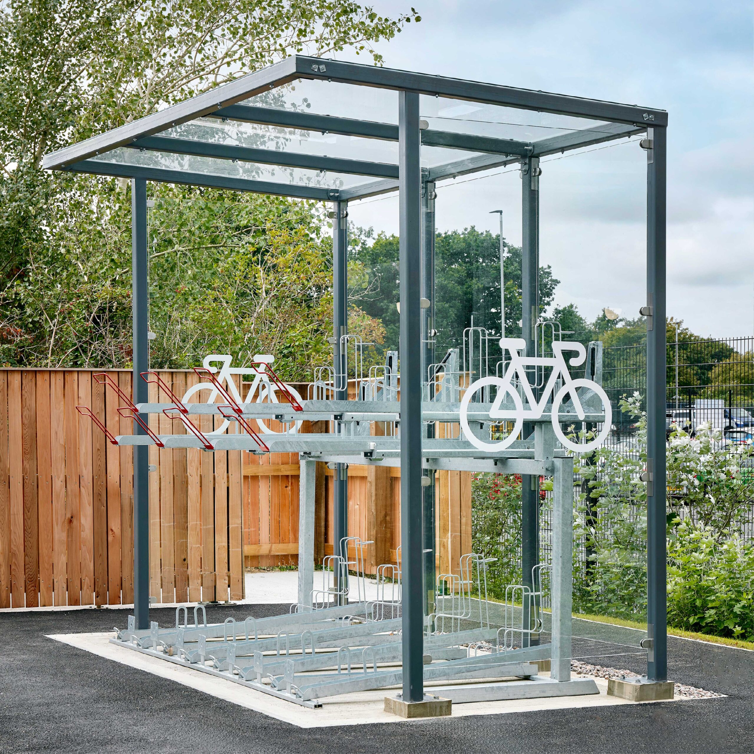 A modern outdoor bicycle parking shelter equipped with secured bike racks and surrounded by greenery and a wooden fence.