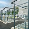 A modern outdoor bicycle parking area with several empty racks under a metal and glass shelter, next to a building with reflective windows.