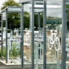 Transparent bike lockers and racks with white bicycle symbols, located in a public parking area for secure bicycle storage.