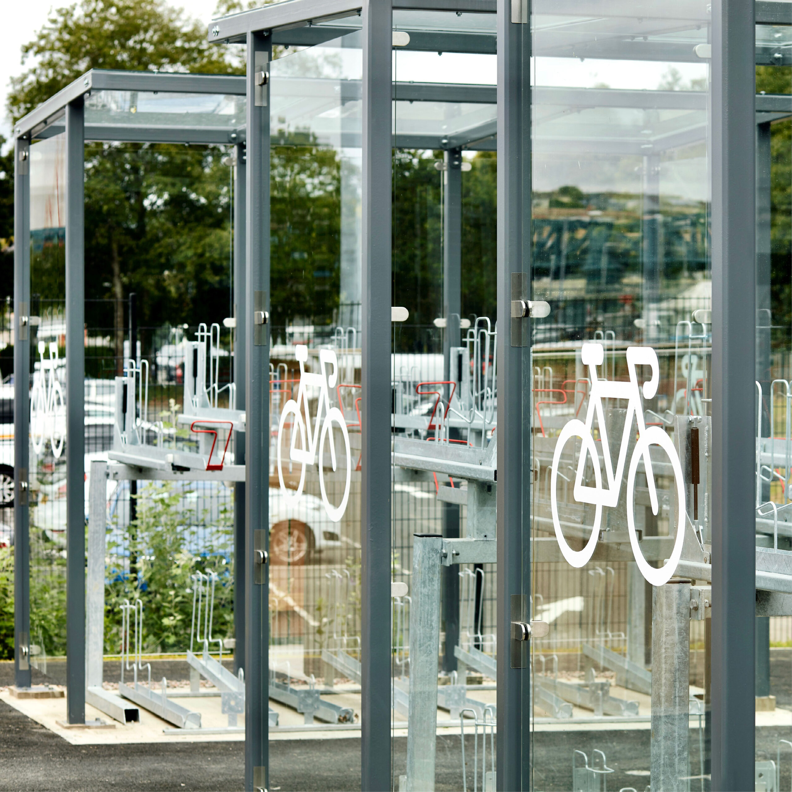 Transparent bike lockers and racks with white bicycle symbols, located in a public parking area for secure bicycle storage.