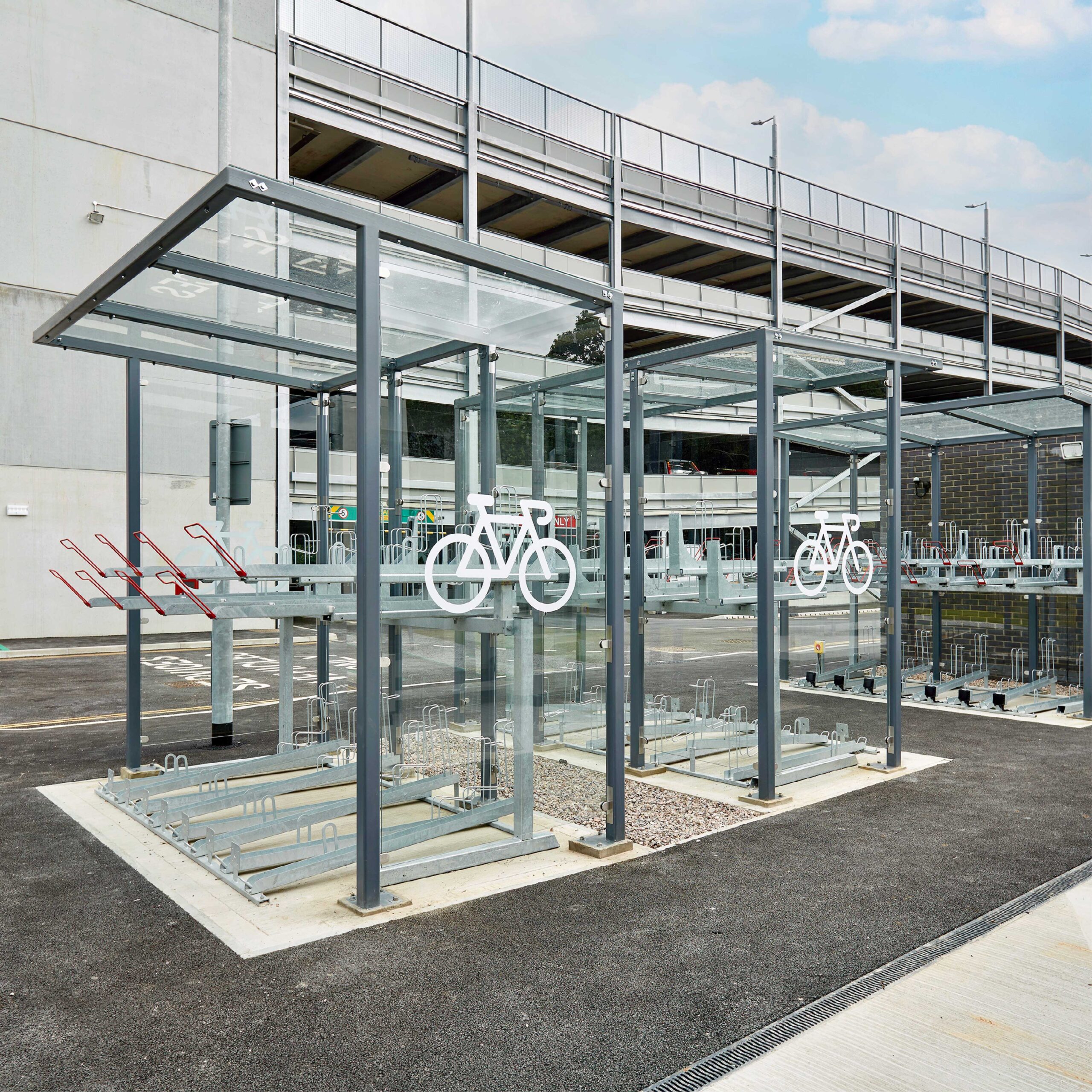 Modern outdoor bicycle parking facility with covered racks and glass windbreaks, designed for secure bike storage, located near a building.