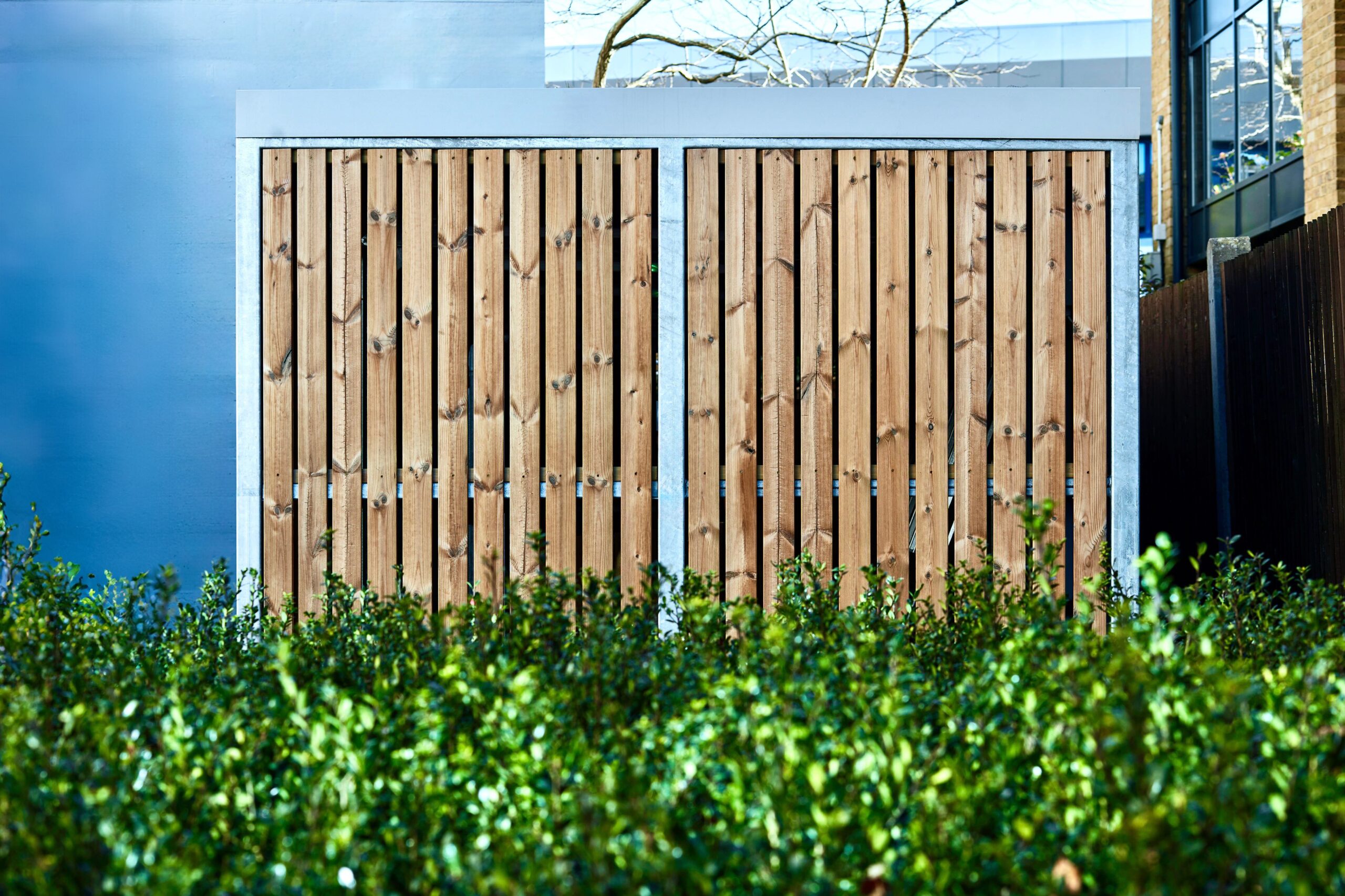 outdoor bike storage with timber cladding behind a a large shrub