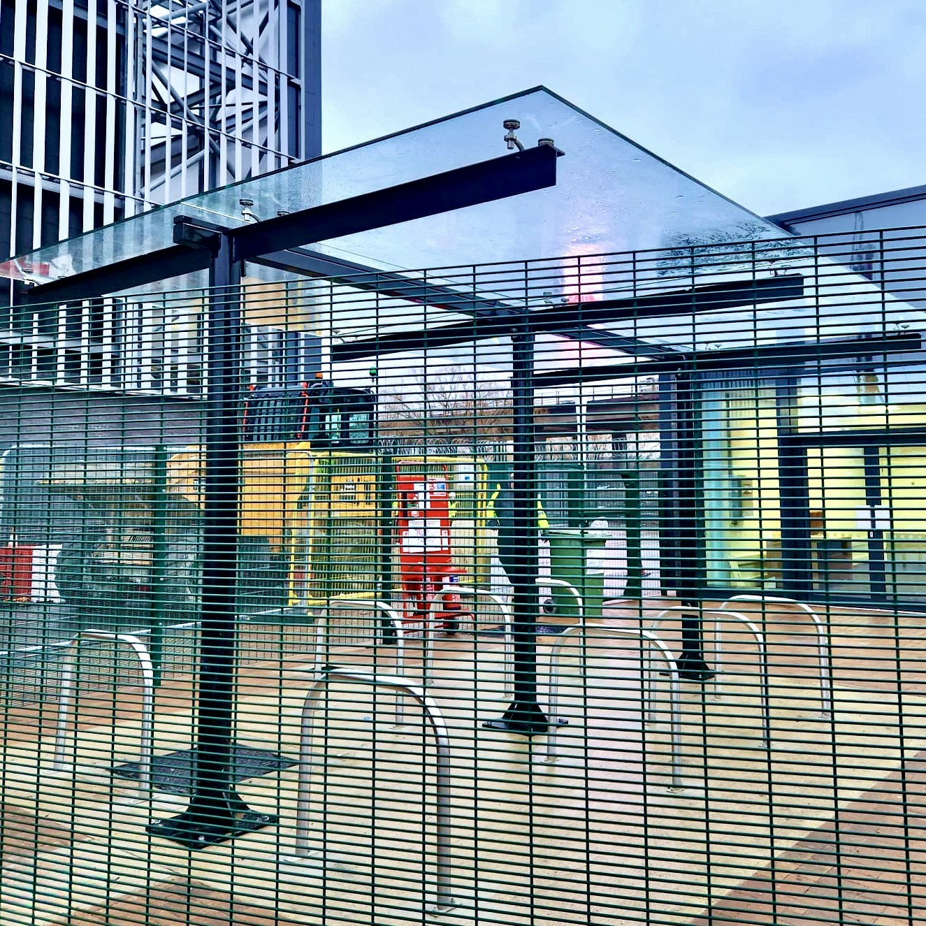 a glass covered bike storage shelter with a metal fence