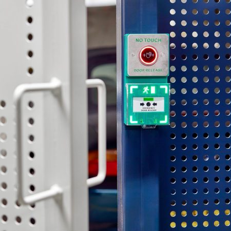 close up of push to exit button on blue and white perforated mesh fencing