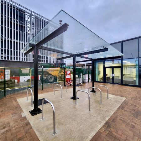 a bike canopy shelter with bike rack with metal bars in front of a building